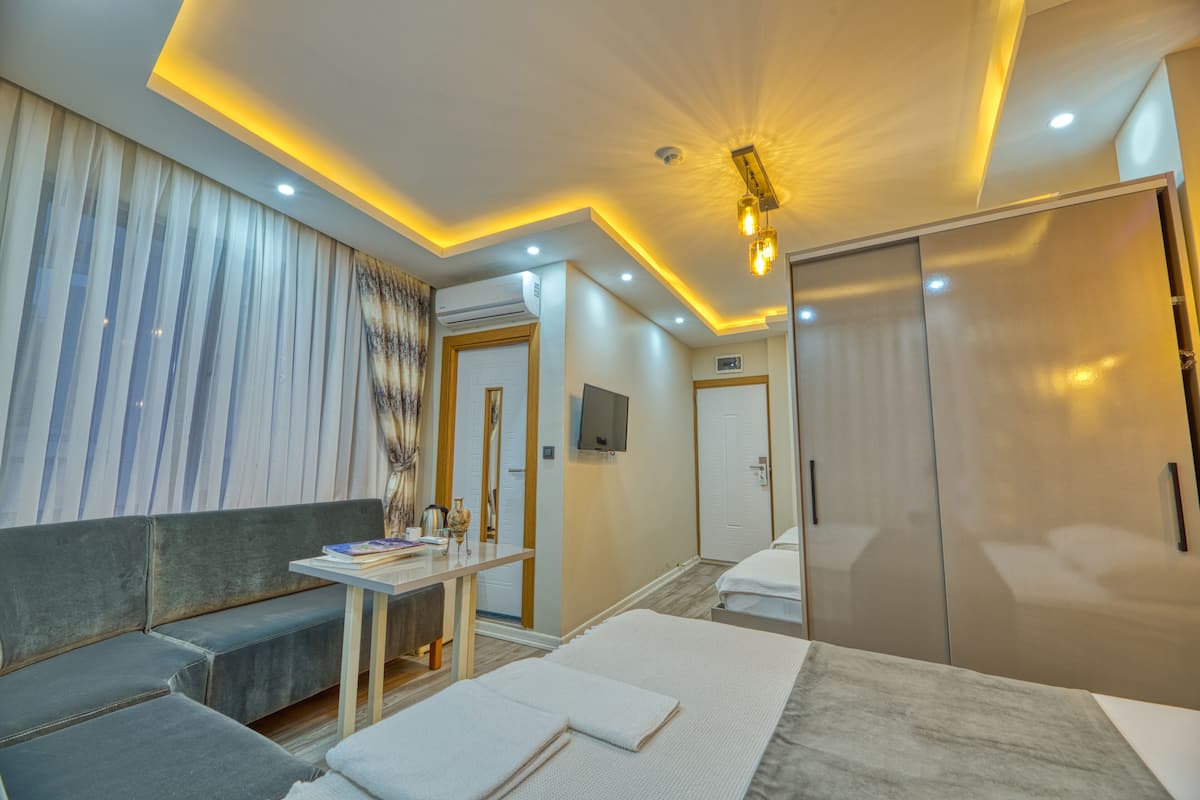 A modern hotel room with a sofa, a small table, a bed with a white headboard, and a wardrobe.