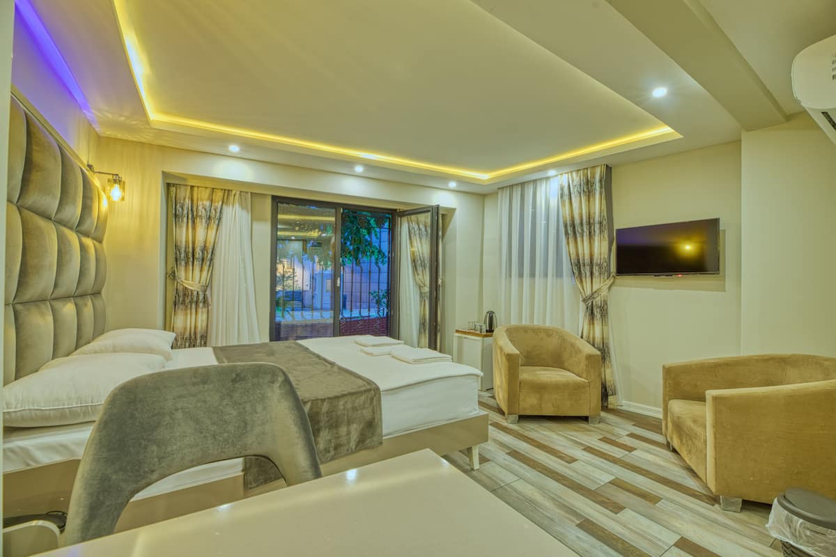 A hotel room with a bed, two armchairs, a TV, and a window with curtains.