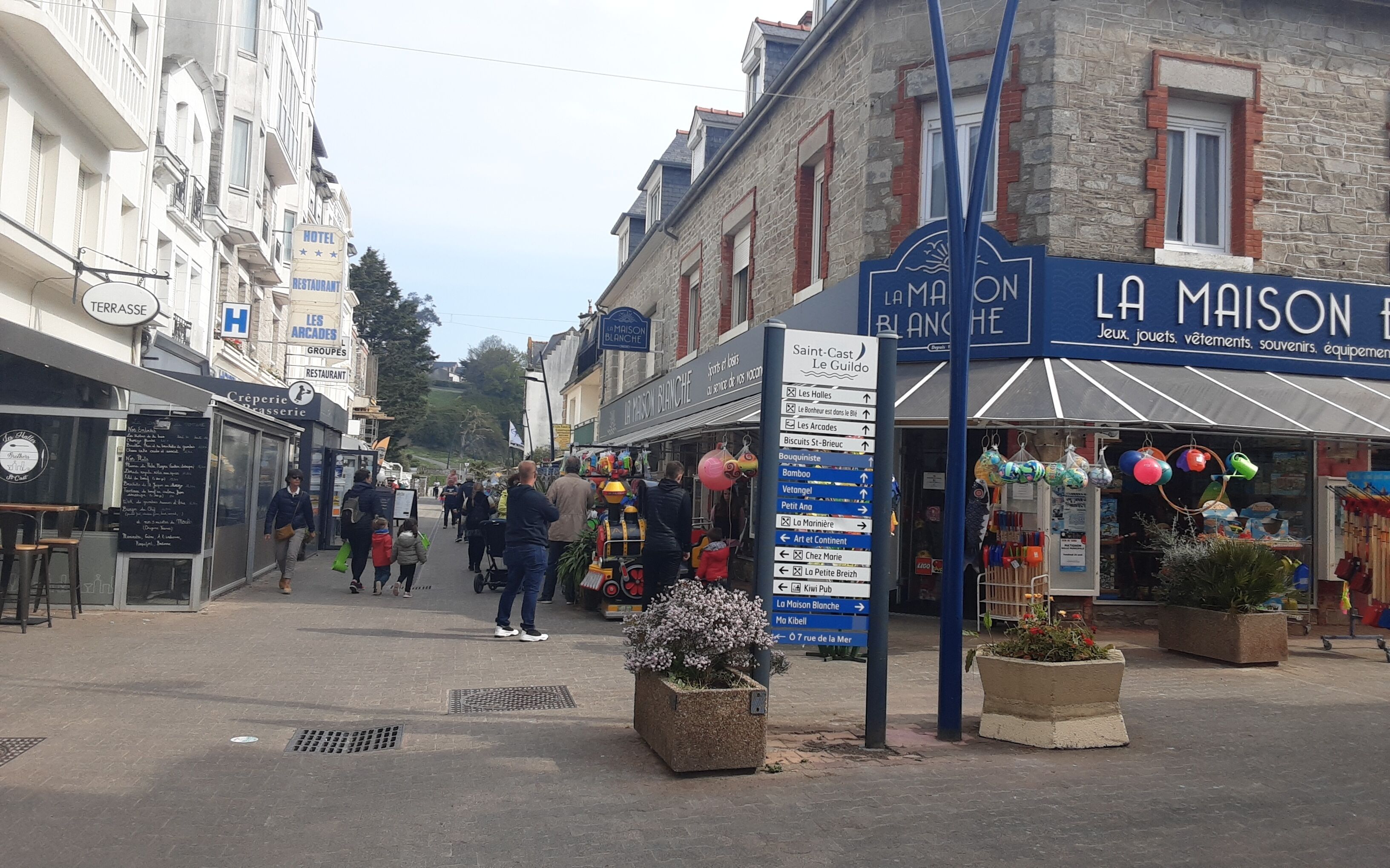 Une vue de rue avec un hôtel appelé « LA MAISON » et un panneau indiquant différentes directions.