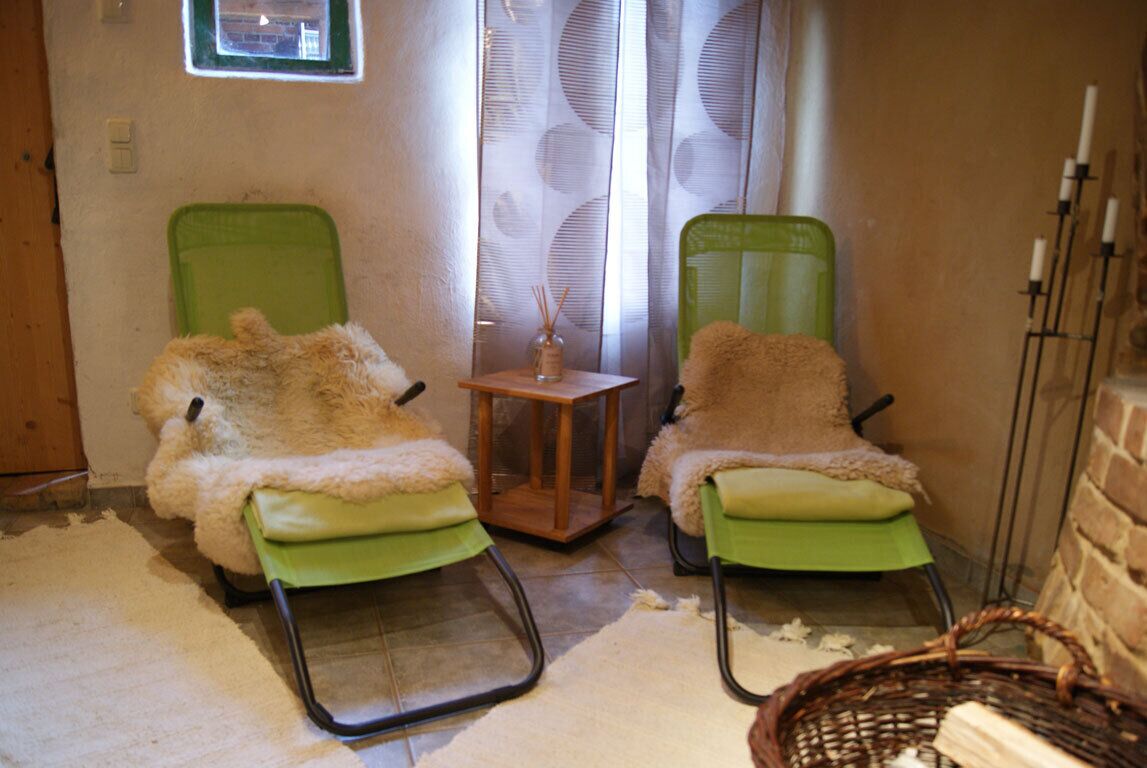 Twee groene stoelen met zachte, beige hoezen, een klein houten tafeltje en een rieten mand.