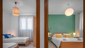 Hotellihuone, jossa on kaksi sänkyä, vihreä seinä ja ikkuna, jossa on läpikuultavat verhot.
