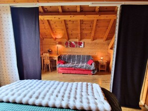 A cozy cabin interior with a wooden ceiling, a sofa, a desk, and a lamp.