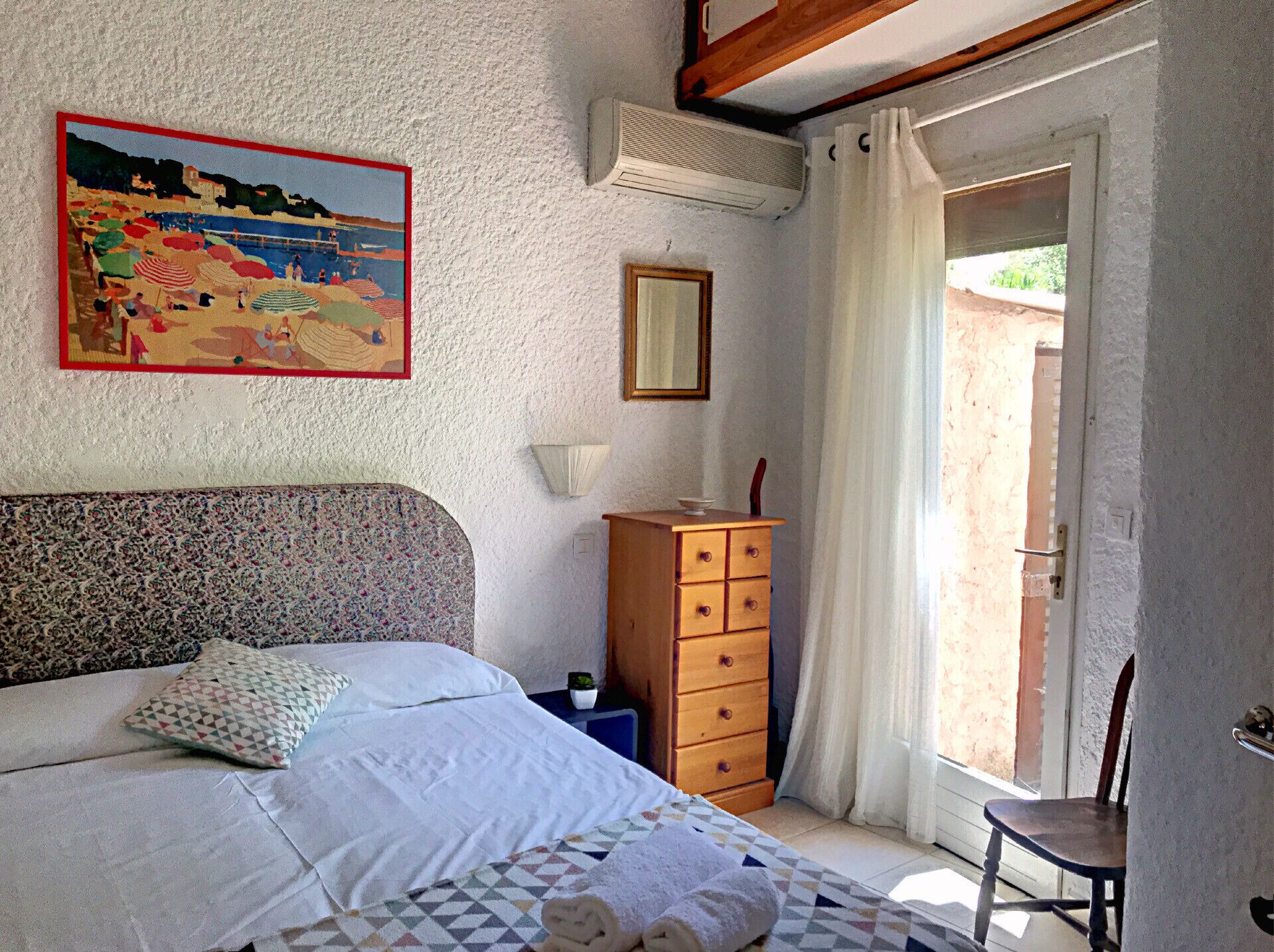 Een slaapkamer met een bed, een dressoir, een schilderij en een raam met gordijnen.