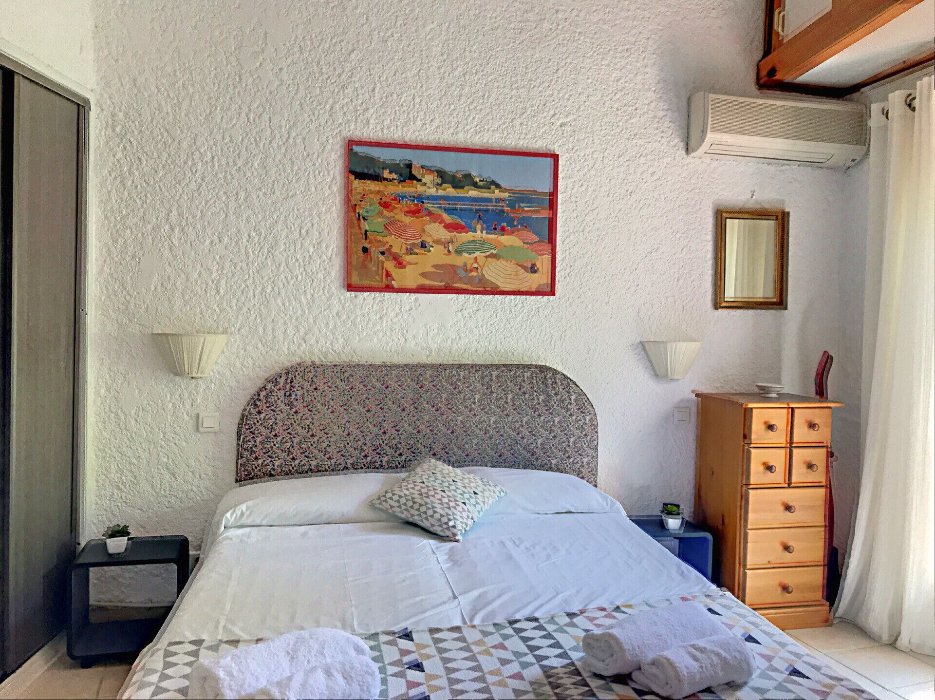 Une chambre à coucher avec un lit, un tableau, une commode et une table de chevet.