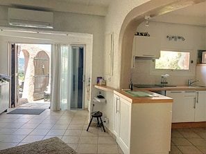 A kitchen with a central island, a dining area with a table and chairs, and a view through an open door to an outdoor area.