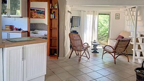 Een kamer met een keuken, een eettafel met stoelen, een televisie en een raam met uitzicht op groen.