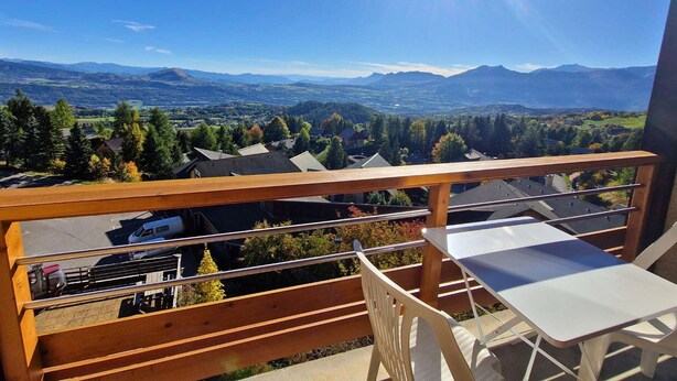 Un balcon offrant une vue sur une vallée, des montagnes et un ciel dégagé.