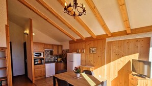 Une cuisine compacte avec des meubles en bois, une table à manger avec des chaises, un four à micro-ondes, un réfrigérateur et un lustre.
