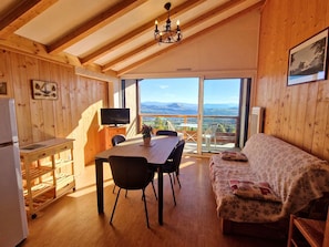 A wooden interior with a dining table, chairs, a sofa, a television, and a view of the outdoors.