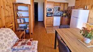 Une pièce chaleureuse avec une bibliothèque en bois, une table à manger et un coin cuisine doté de meubles et d’appareils électroménagers en bois.
