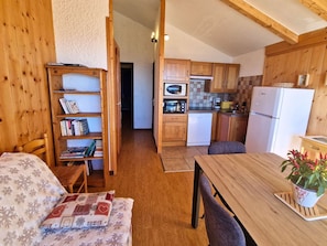 Une pièce chaleureuse avec une bibliothèque en bois, une table à manger et un coin cuisine doté de meubles et d’appareils électroménagers en bois.