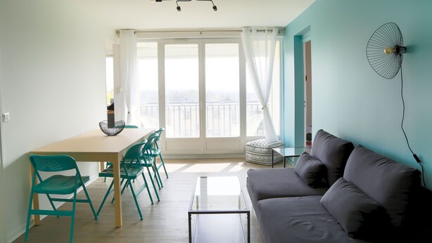 A living room with a sofa, a dining table with chairs, a coffee table, and a ceiling fan.