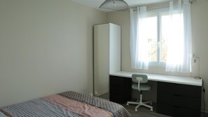 A bedroom with a bed, a desk, a chair, a wardrobe, and a window with curtains.