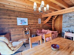 L’intérieur chaleureux d’un chalet avec une table à manger en bois, des sièges confortables, une cheminée et un mur en pierre.