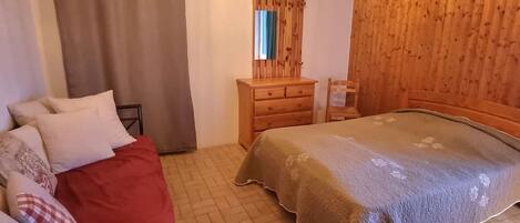 A bedroom with a bed, a wooden dresser, a mirror, and a window with curtains.