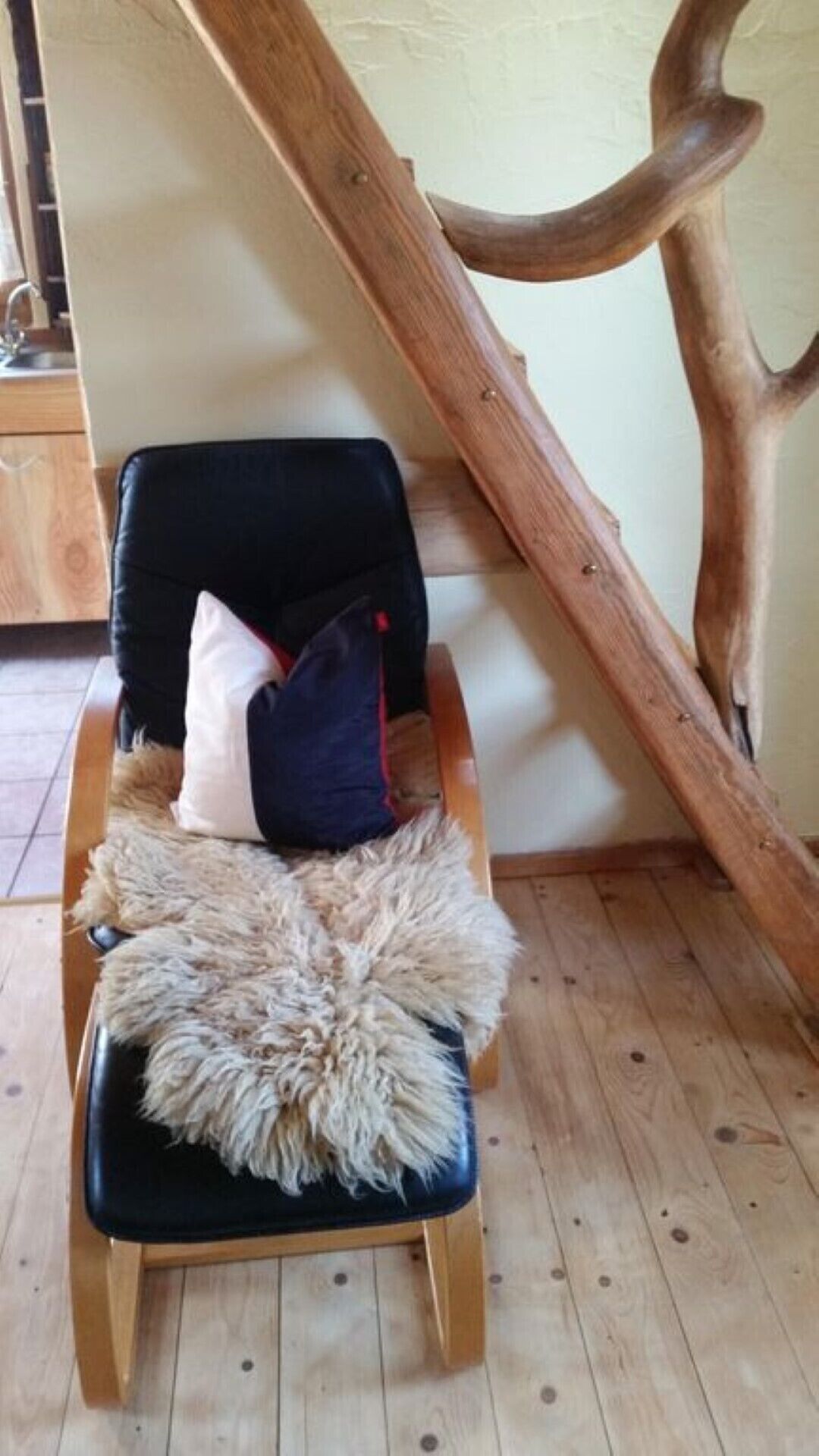 A chair with a fur throw and pillows, positioned in a room with wooden flooring and a large wooden beam structure.