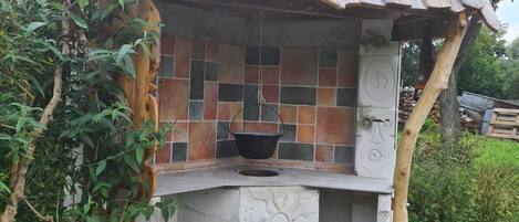 A rustic outdoor cooking area with a tiled backsplash, a black pot on the counter, and a stone foundation.