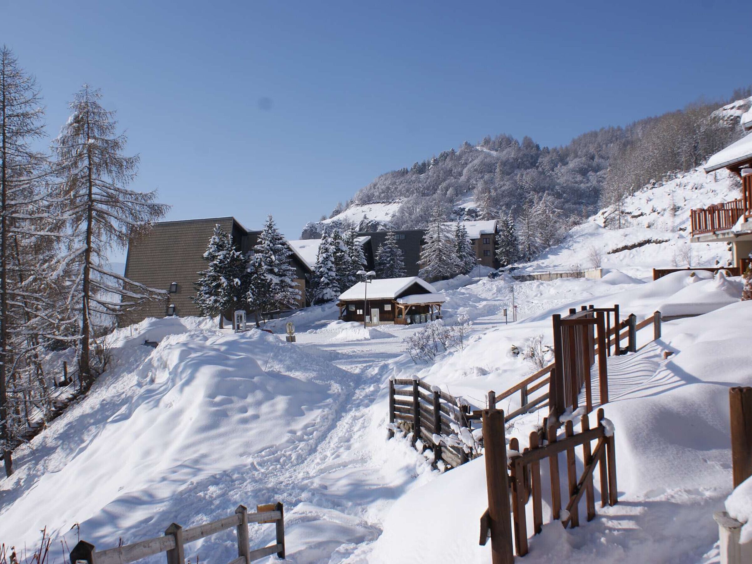 A snow-covered ski resort with wooden cabins, a ski lift, and a mountain backdrop.
