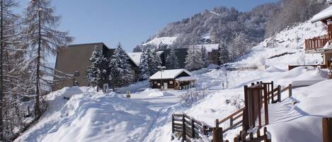 A snow-covered ski resort with wooden cabins, a ski lift, and a mountain backdrop.