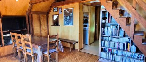 Un interior de madera con una mesa de comedor, sillas, una estantería y una escalera.