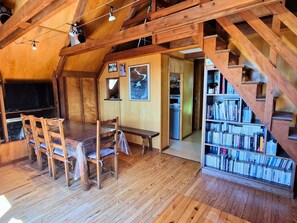 Ein Holzinnenraum mit Esstisch, Stühlen, B ücherregal und einer Treppe.