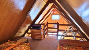 Une chambre mansardée chaleureuse, avec deux lits, une commode en bois et une échelle.