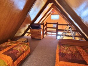 A cozy attic bedroom with two beds, a wooden dresser, and a ladder.