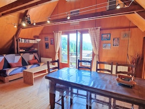 A cozy room with a wooden ceiling, a dining table, a sofa, and a bookshelf.