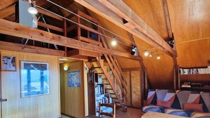 Une pièce mansardée avec des poutres en bois, un escalier, un canapé, une table et une bibliothèque.
