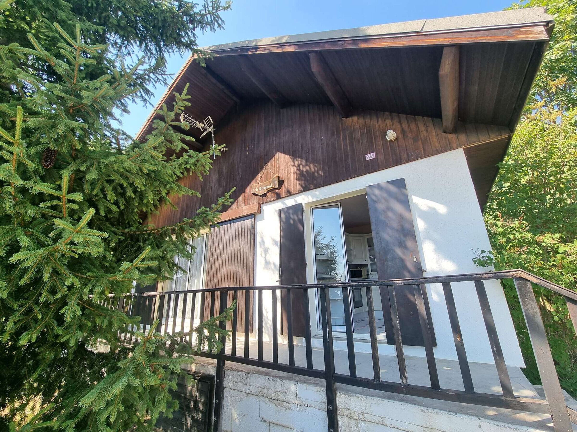 A modern building with a wooden exterior, a balcony with a metal railing, and a door leading to an interior space.