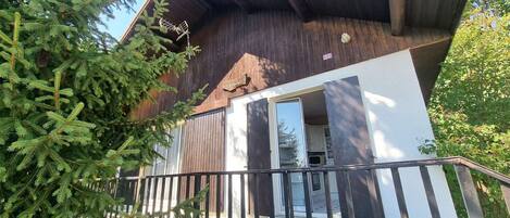 A modern building with a wooden exterior, a balcony with a metal railing, and a door leading to an interior space.