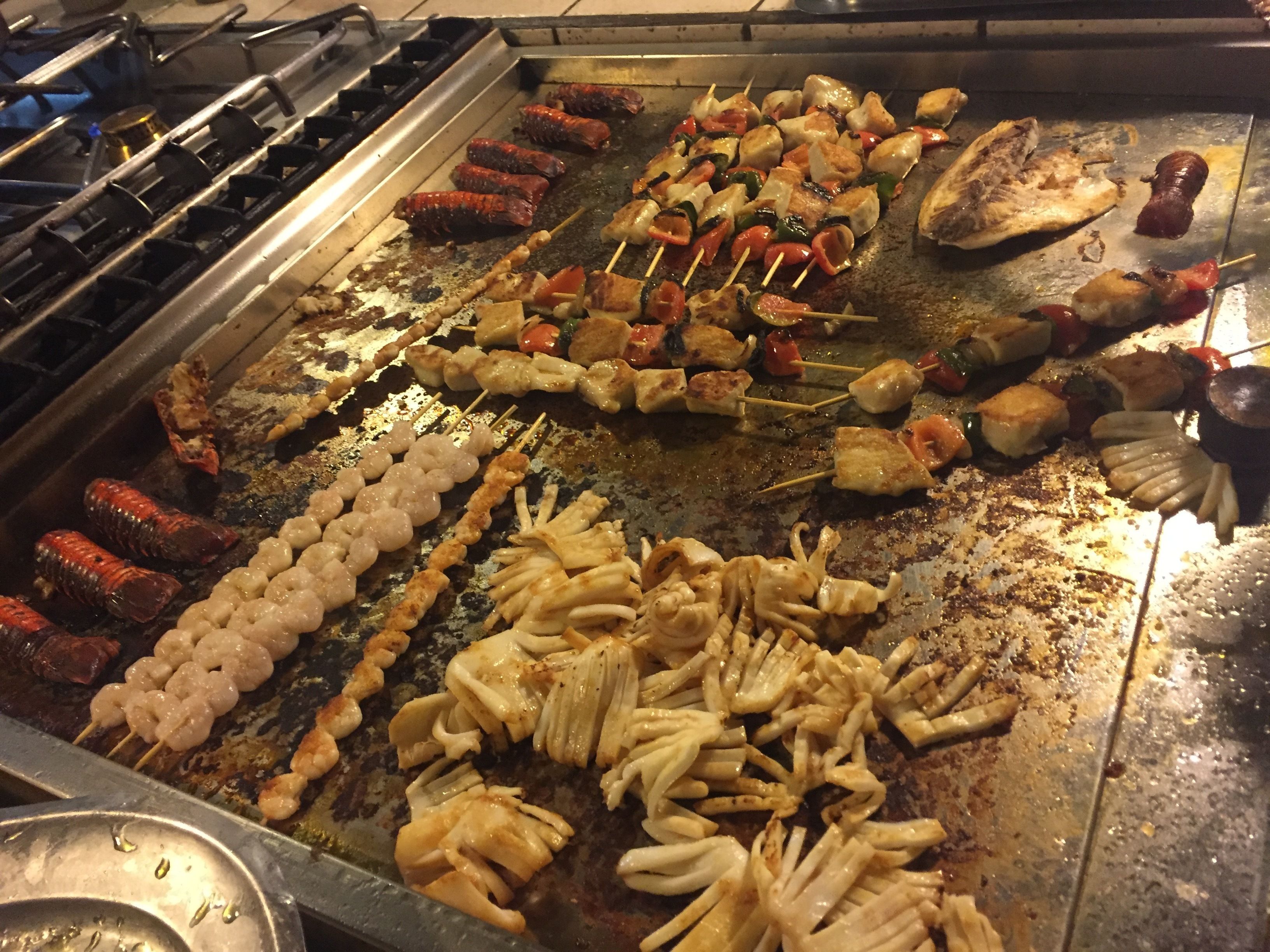 Diversos cortes de carne grelhada e vegetais em uma churrasqueira grande.