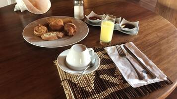 Une table en bois dressée pour le petit-déjeuner, avec des croissants, une tasse de café, un verre de jus d’orange et divers condiments.