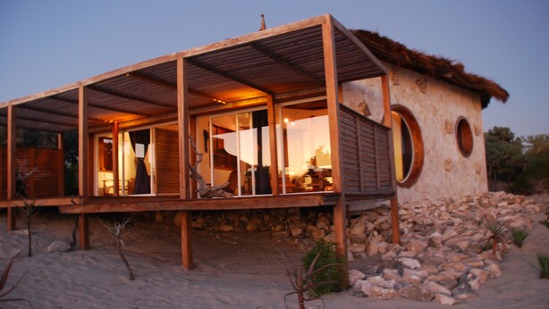 Una casa moderna frente a la playa con terraza de madera, ventanas amplias y fachada de piedra.