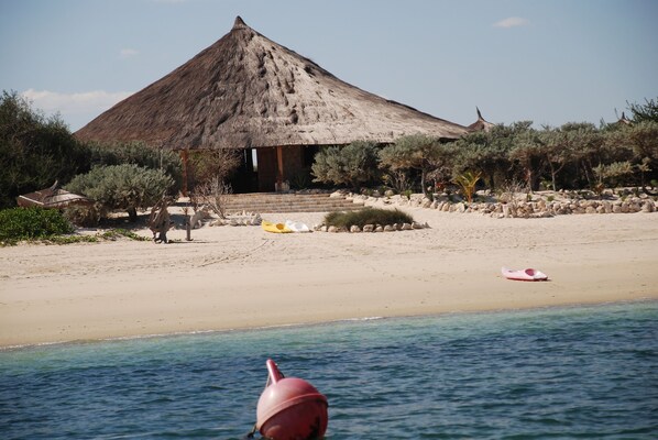 A beach with a thatched-roof building, clear blue water, and a buoy in the foreground. - Anakao Ocean Lodge & Spa (Anakao)