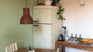 A compact kitchen with a wooden table, a white refrigerator, a clock on the wall, and a hanging pendant light. - B&B Colombo (Mestre)