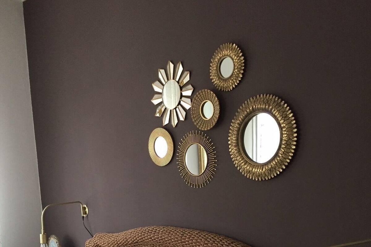 A bedroom with a brown headboard, a bed with patterned bedding, and multiple wall mirrors.
