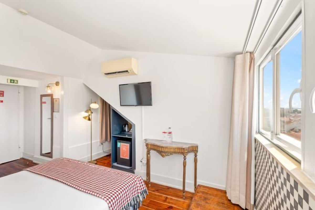 A hotel room with a bed, a small table, a TV, and a window with a view.