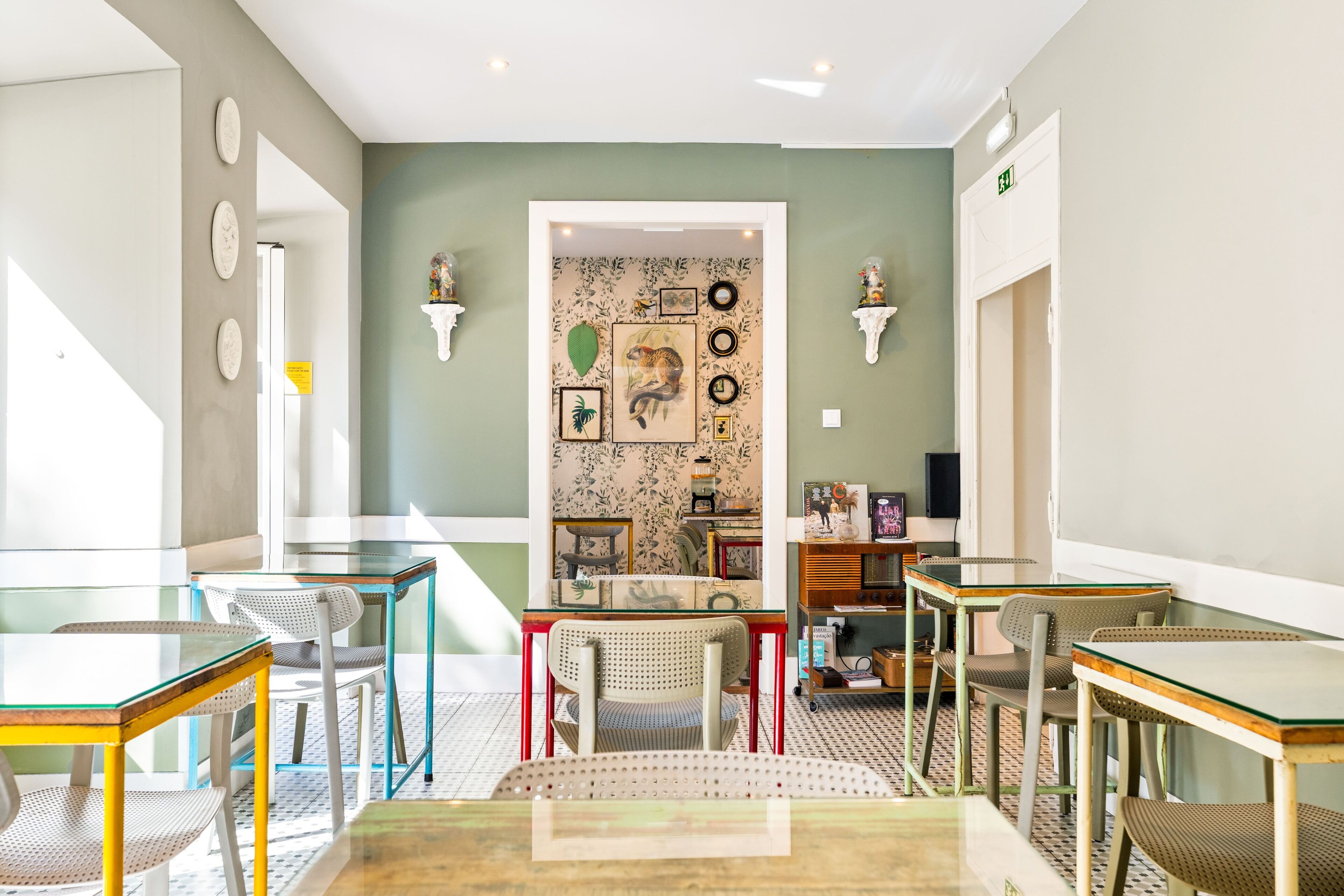 Een kamer met een groene accentmuur, een centraal zithoek met stoelen en tafels, en een decoratieve muur met ingelijste foto’s en spiegels.
