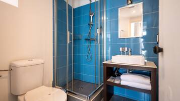 Un baño moderno con ducha de vidrio, inodoro blanco y lavamanos con espejo.