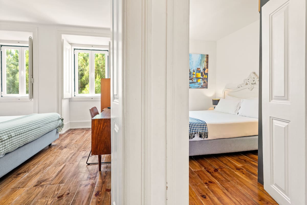 Een kamer met een bed, een bureau en een stoel. Er zijn ramen met uitzicht op groen.
