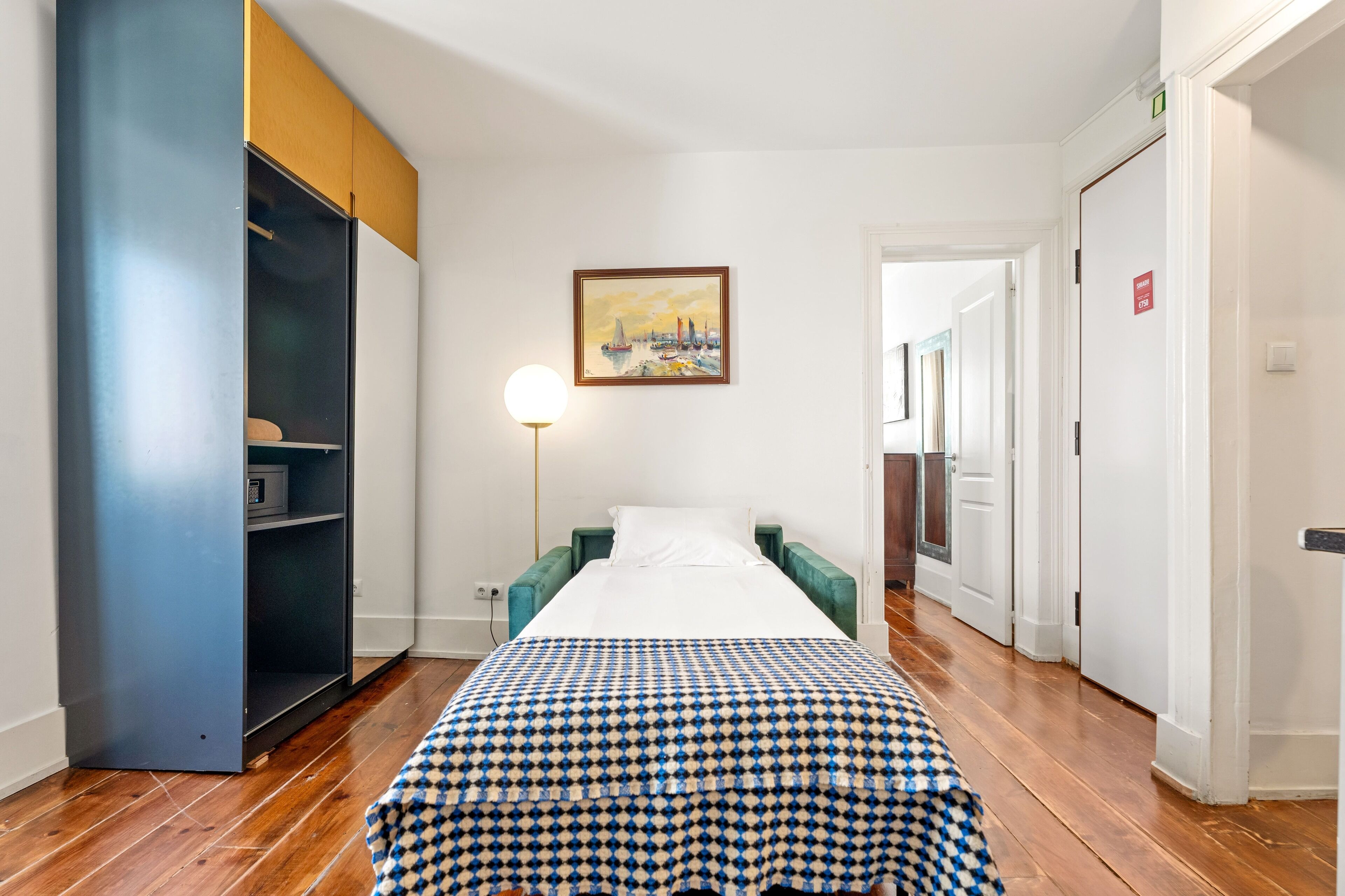 A hotel room with a bed, a wardrobe, a painting, and a lamp.