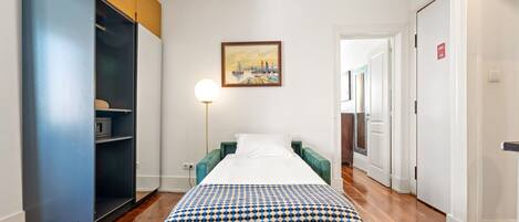 A hotel room with a bed, a wardrobe, a painting, and a lamp.