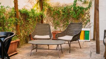 A patio with wicker chairs and a table, surrounded by potted plants and a lattice wall.