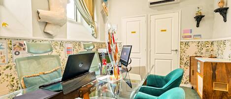 A room with a glass table, two laptops, teal chairs, a wooden cabinet, and a wall-mounted sculpture.
