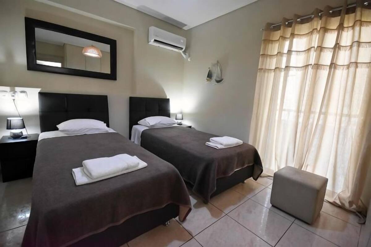 Een hotelkamer met twee bedden, een nachtkastje, een spiegel, een airconditioner en een raam met gordijnen.