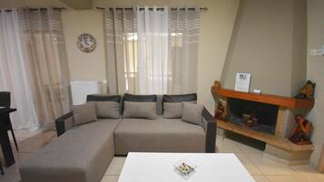 A living room with a beige sofa, a white coffee table, a fireplace, and sheer curtains.