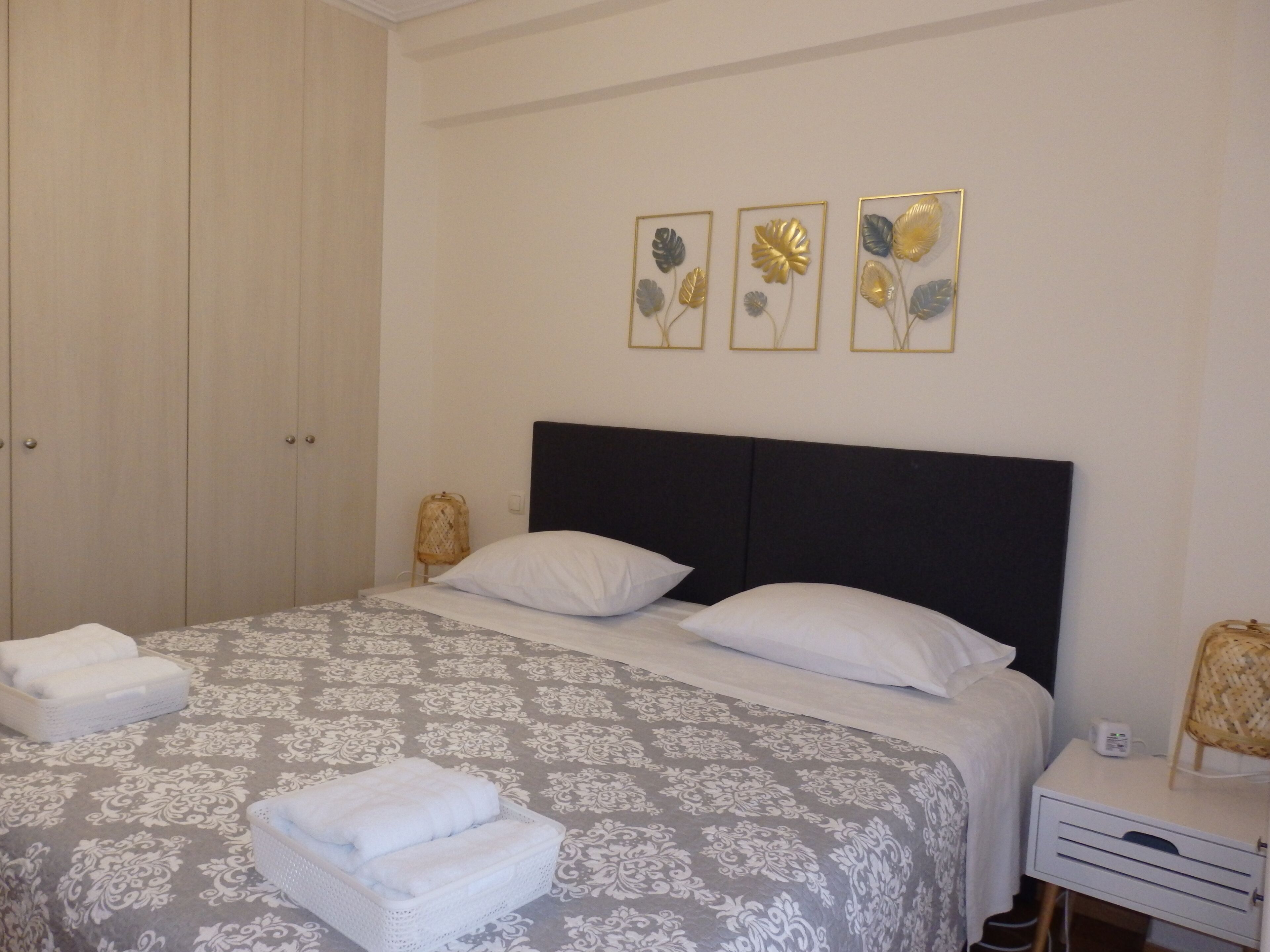 A neatly made bed with a patterned bedspread, two pillows, and folded towels on the side. There are three wall-mounted decorative pieces above the bed.