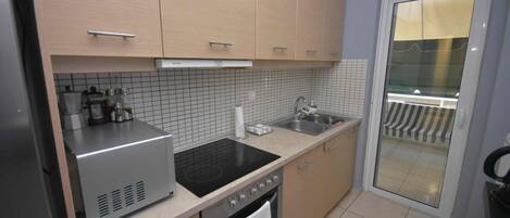 A modern kitchen with light wood cabinets, a stainless steel range, a black induction cooktop, and a tiled backsplash.