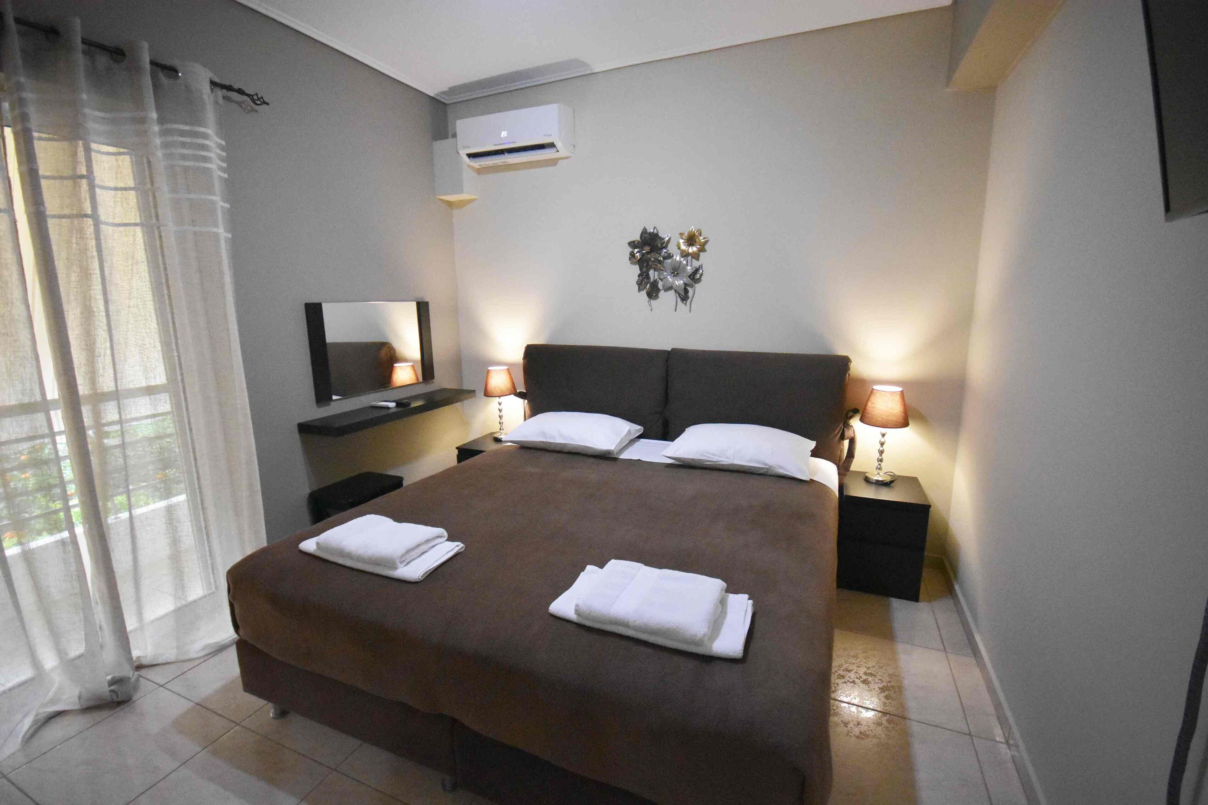 A hotel room with a large bed, two bedside tables with lamps, a flat-screen TV, and a wall-mounted air conditioner.